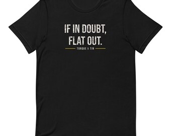 May include: A black short-sleeve t-shirt featuring the white distressed text IF IN DOUBT, FLAT OUT. centered on the chest. Below the text is a thin horizontal gold line with the words TORQUE & TIN printed in white underneath the line.