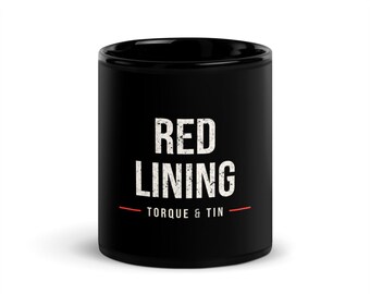 May include: A black ceramic mug featuring the white distressed text RED LINING centered on the front. Below this, the text TORQUE & TIN appears in smaller white letters, flanked by two thin horizontal red lines on either side.