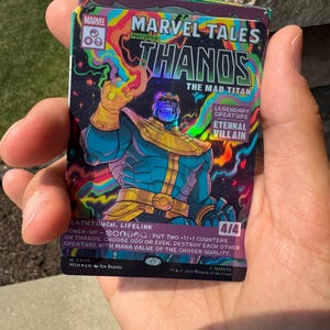 May include: A Marvel Tales trading card featuring Thanos the Mad Titan with a holographic finish. The card displays colorful swirling patterns, the character in armor with an Infinity Gauntlet, and text including Legendary Creature, Eternal Villain, and 4/4.