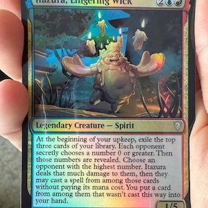 May include: A holographic Magic: The Gathering trading card titled Itazura, Lingering Wick. The card features a central illustration of a wax-like creature with candles on its head, set against a dark, atmospheric background with blue and red borders.