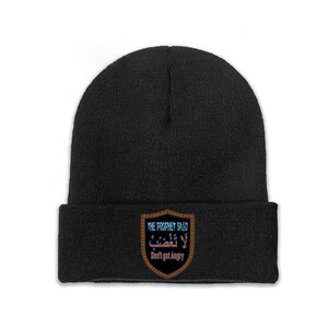 Puede incluir: Un gorro de punto negro con un parche en forma de escudo en el dobladillo frontal. El parche tiene un borde marrón y muestra el texto "THE PROPHET SAID", escritura árabe y la traducción "Don't get Angry" en una fuente estilizada.