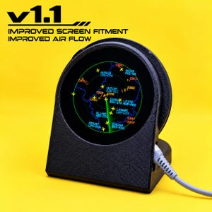 Puede incluir: Una unidad de pantalla electrónica circular negra con una interfaz de radar con datos de vuelo, el texto v1.1 IMPROVED SCREEN FITMENT IMPROVED AIR FLOW y un cable de alimentación gris conectado al lateral, sobre un fondo amarillo sólido.