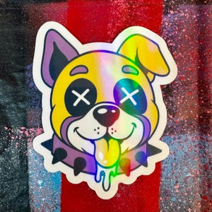 Op de afbeelding: Een holografische sticker met een cartoon hondenkop met gele vacht, paarse oren en zwarte X-vormige ogen. De hond draagt een paarse halsband met stekels en steekt zijn tong uit met een druipend effect, uitgevoerd in een levendige afwerking.