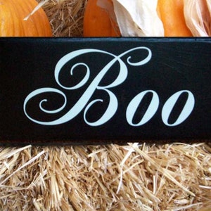 K&ouml;nnte beinhalten: Schwarzes Holzschild mit wei&szlig;er, geschwungener Schrift, auf dem "Boo" steht, auf einem Hintergrund aus Heu.