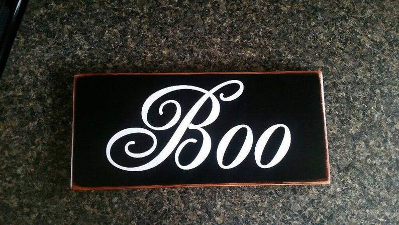 K&ouml;nnte beinhalten: Ein schwarzes Holzschild mit einer wei&szlig;en kursiv geschriebenen Aufschrift "Boo".