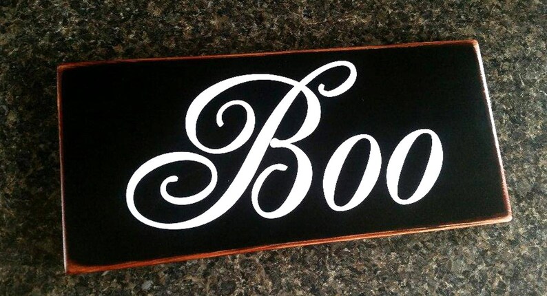 K&ouml;nnte beinhalten: Schwarzes Holzschild mit einem wei&szlig;en, kursiv geschriebenen "Boo".