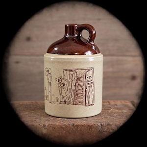 May include: A ceramic jug with a glossy brown glazed top and a matte beige base. The body features a brown line drawing of two figures embracing near a barn door, with the text "ΔZ BARN PARTY 1978" printed on the side of the open barn structure.