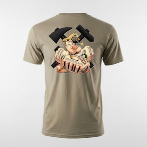 Può includere: Una t-shirt a maniche corte color marrone chiaro con una grafica sul retro raffigurante un personaggio marinaio dei cartoni animati con un cappello, posizionato davanti a due martelli neri incrociati. La grafica include il testo "UNITED STATES NAVY CHIEF" e "1775/1893".