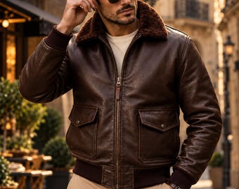 May include: A dark brown leather bomber jacket featuring a plush brown faux fur collar, a central metal zipper, two front flap pockets with snap buttons, and ribbed knit cuffs and hem. The ORIXO LEATHER logo is visible in the top left corner.