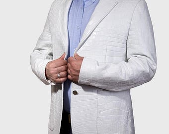 May include: A white blazer featuring a textured crocodile skin pattern, a notched lapel, and two front patch pockets. The blazer is worn over a light blue button-down shirt. The jacket is fastened with a single metallic button at the center front.
