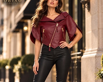 May include: A deep burgundy leather jacket featuring short, flared sleeves, an asymmetrical front zipper closure, and two zippered pockets. The jacket is paired with black fitted trousers. The ORIXO LEATHER logo is visible in the top left corner.