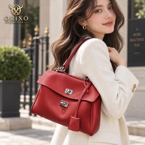 May include: A red leather handbag featuring a top handle, a fold-over flap with a silver-toned metal turn-lock closure, and a matching leather luggage tag hanging from the side. The ORIXO LEATHER logo is visible in the upper left corner.