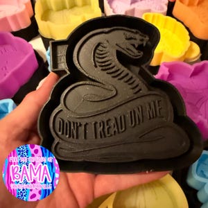 May include: A black plastic cookie cutter shaped like a coiled snake with its mouth open. The design features the text "DONT TREAD ON ME" embossed across the body of the snake. The cutter has a thick frame and a textured surface from the 3D printing process.
