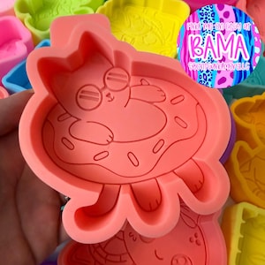 May include: A coral-colored silicone mold featuring an embossed design of a cat wearing sunglasses while floating in a donut-shaped inner tube. The mold includes a circular sticker with the text Find me on Etsy at BAMA SCENTSANDMORELLG.