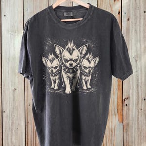 Könnte beinhalten: Ein anthrazitfarbenes Kurzarm-T-Shirt mit einem Grafikdruck von drei kleinen Hunden mit stacheligen Irokesenschnitten und Stachelhalsbändern. Die Hunde sind in einem hellen Cremeton auf dem dunklen Stoff des Shirts abgebildet.