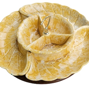 Könnte beinhalten: Eine gelbe Keramik-Servierplatte mit einem geteilten Mittelteil und drei separaten Schalen. Die Platte hat einen gewellten Rand und einen Holzsockel.
