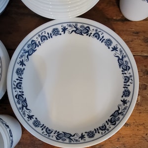 Puede incluir: Juego de vajilla de cerámica blanca con un diseño de borde floral azul. El juego incluye platos, cuencos y tazas. Los platos tienen un diámetro de aproximadamente 25 cm. Las tazas y los cuencos también son blancos con detalles florales azules.