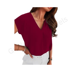 Könnte beinhalten: Eine kurzärmelige Bluse in tiefem Burgunderrot mit V-Ausschnitt, kombiniert mit einer weißen Hose. Die Bluse hat eine lockere Passform und besteht aus einem glatten, einfarbigen Stoff. Das Outfit wird durch eine zarte Goldkette ergänzt.