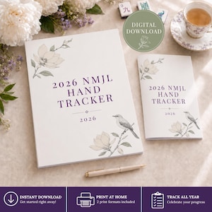 May include: Two white booklets titled 2026 NMJL HAND TRACKER in purple text, featuring illustrations of magnolia flowers and a bird on a branch. A light-colored pen lies horizontally below the larger booklet, which is accompanied by a tea cup.