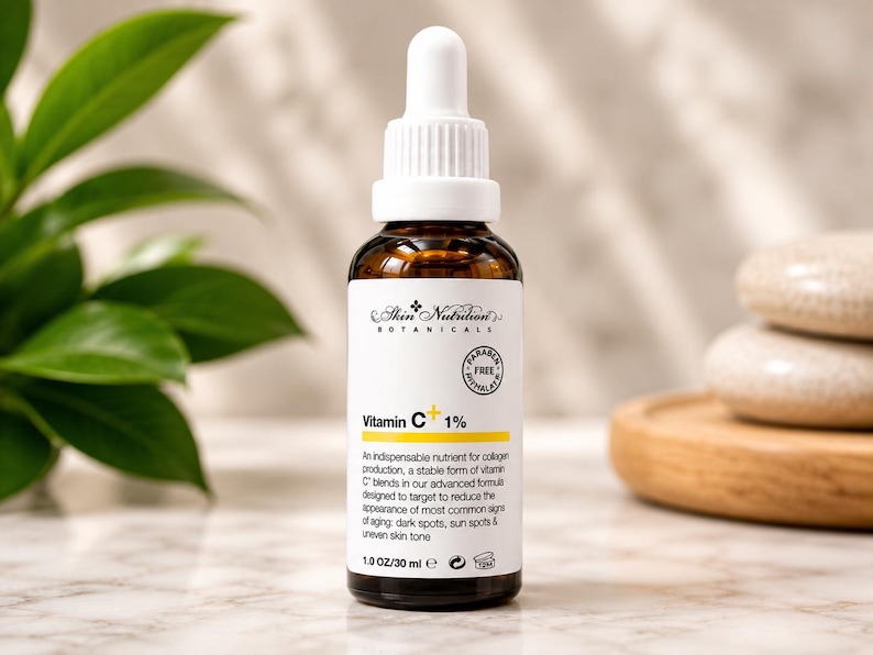 K&ouml;nnte beinhalten: Eine braune Glastropfflasche mit Skin Nutrition Botanicals Vitamin C+ 1% Serum. Das wei&szlig;e Etikett zeigt schwarzen Text, eine gelbe Akzentlinie und ein kreisf&ouml;rmiges Paraben Free Phthalate Free Siegel. Die Flasche enth&auml;lt 30 ml Fl&uuml;ssigkeit.