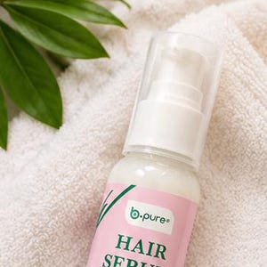 May include: A clear plastic pump bottle of b.pure hair serum with a pink and green label. The label features the text HAIR SERUM, CURL DEFINING, and moisturizes and defines curls in dark green and white lettering against a light background.
