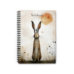 May include: Spiral-bound notebook featuring an illustration of a hare with long ears, a small figure atop its head, and a warm-toned sun in the background. The notebook has text that reads "Notebook Brambledash the Swift Whisper".