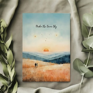 May include: A rectangular art print featuring a watercolor landscape with a couple silhouetted against a sunset. The text "Under the Same Sky" is written across the top. The color palette includes blues, oranges, and browns.