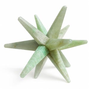 Könnte beinhalten: Eine sternförmige Skulptur mit mehreren Spitzen, die aus hellgrünem Stein gefertigt ist. Das Objekt besteht aus zahlreichen länglichen, spitz zulaufenden Strahlen, die von einem Kern ausgehen und natürliche mineralische Maserungen aufweisen.