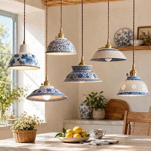 May include: Five hanging pendant lights with white ceramic shades featuring blue floral patterns and intricate cut-out designs. Each lamp has a brass-toned fixture and a twisted brown cord, suspended above a table with a bowl of lemons.