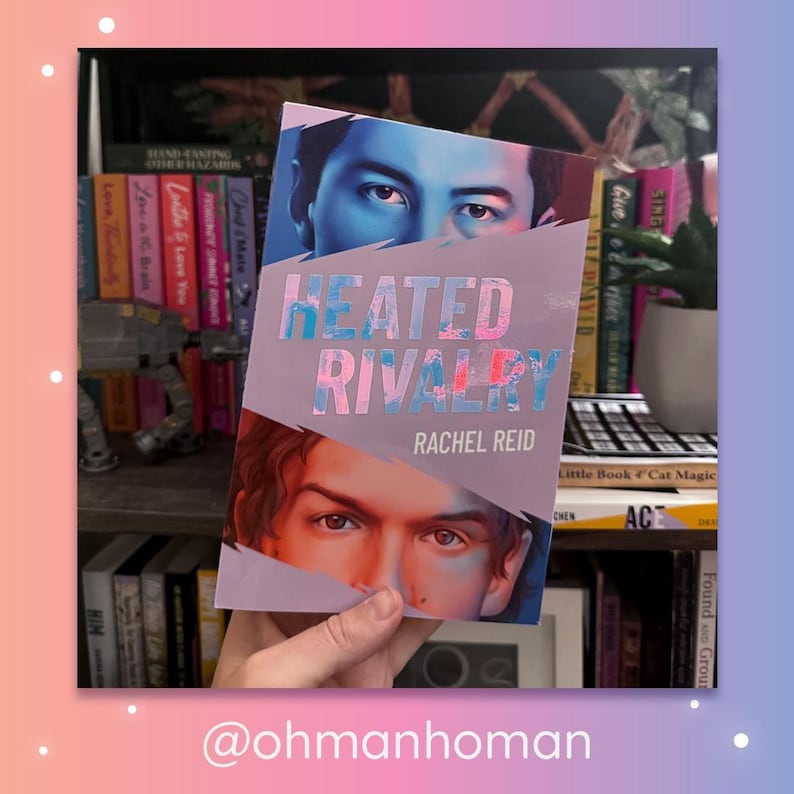 May include: A paperback book titled Heated Rivalry by Rachel Reid. The cover features a split design with a person's eyes in blue tones at the top and another person's eyes in warm tones at the bottom, separated by a jagged white diagonal line.