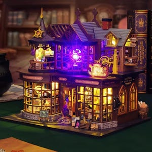 Puede incluir: Una maqueta en miniatura de una tienda de magia de varios pisos con exterior morado oscuro y marrón y ventanas iluminadas. La estructura muestra letreros que dicen Magic Treasure House y Magic Shop, con una luz morada brillante en el centro.