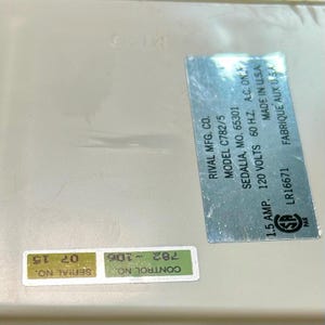 May include: A white appliance base featuring a silver metallic label with black text: RIVAL MFG. CO. MODEL C782/5 SEDALIA, MO. 65301 120 VOLTS 60 H.Z. A.C. ONLY 1.5 AMP. MADE IN U.S.A. LR16671. Includes a green sticker with SERIAL NO. 07 15 and CONTROL NO. 782-106.