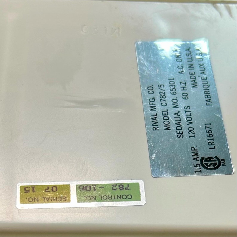 May include: A white appliance base featuring a silver metallic label with black text: RIVAL MFG. CO. MODEL C782/5 SEDALIA, MO. 65301 120 VOLTS 60 H.Z. A.C. ONLY 1.5 AMP. MADE IN U.S.A. LR16671. Includes a green sticker with SERIAL NO. 07 15 and CONTROL NO. 782-106.
