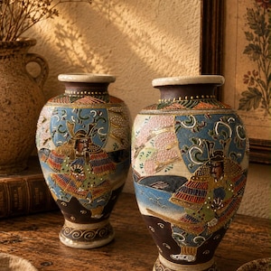 May include: Two ceramic vases featuring raised, colourful depictions of samurai warriors in traditional armour. The vases have a dark brown base, a light-coloured rim, and intricate painted details in blue, red, and gold, showcasing a textured finish.