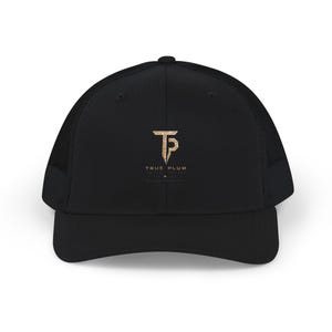 May include: A black trucker hat featuring a mesh back and a solid front panel. Centered on the front is a gold-colored logo consisting of the letters TP in a stylized font, with the text TRUE PLUM printed in gold lettering directly below the logo.