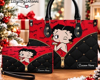Op de afbeelding: Een rood en zwart handtas- en portemonneeset met een Betty Boop-afbeelding, goudkleurige ritsen, doorgestikte zwarte panelen met gouden studs, zwarte handvatten en een label voor een aangepaste naam rechtsonder op elk item.
