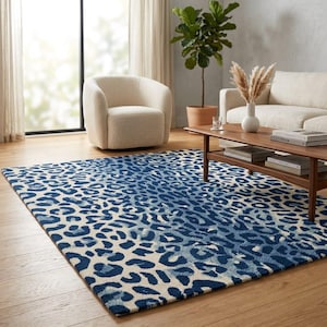 May include: A rectangular area rug featuring a repeating leopard print pattern in shades of deep blue and off-white. The rug is laid flat on a wooden floor, covering a large portion of the visible space in front of a chair and sofa.
