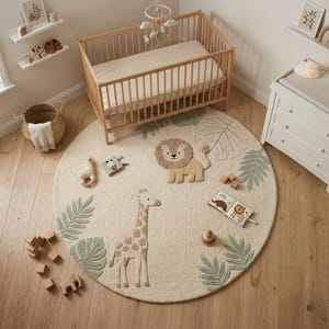 May include: A large, round, cream-coloured area rug featuring a tufted lion and giraffe design in the centre, surrounded by sage green palm leaf motifs. The rug is placed on a light wood floor, with various small wooden toys scattered around it.