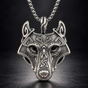 May include: A silver-toned metal pendant shaped like a wolf head, featuring intricate engraved geometric and knotwork patterns. The pendant is suspended from a matching silver-toned box chain necklace with a polished, metallic finish.
