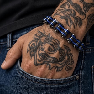 May include: A bracelet constructed from interconnected metal links that resemble a motorcycle drive chain. The design features alternating black and metallic blue segments, with small silver-toned rivets securing each individual link together.
