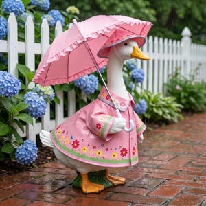 May include: A white goose figurine wearing a pink raincoat with a floral pattern and a matching pink rain hat. The goose holds a pink ruffled umbrella with a white handle. The figure stands on a green base, showcasing a detailed outdoor design.