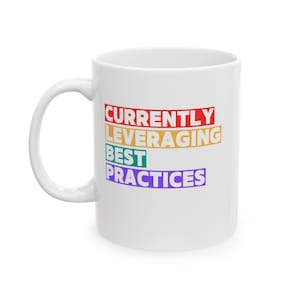 Könnte beinhalten: Ein weißer Keramikbecher mit dem Text "CURRENTLY LEVERAGING BEST PRACTICES", der in vier Zeilen untereinander gedruckt ist. Das Wort "CURRENTLY" ist rot, "LEVERAGING" orange, "BEST" grün und "PRACTICES" lila, jeweils auf farbigem Hintergrund.