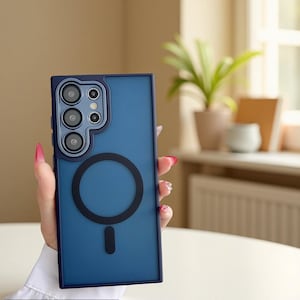 May include: A rectangular dark blue smartphone case featuring a matte finish, a raised camera cutout with multiple circular lens openings, and a prominent black circular magnetic ring design centered on the back panel for wireless charging.