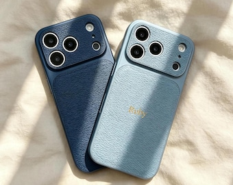 May include: Two smartphone cases with a textured, leather-like finish. One case is dark navy blue, and the other is a lighter dusty blue with the name Ruby embossed in gold lettering. Both feature a raised camera module with three circular lenses.