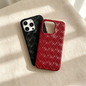 Può includere: Due custodie per smartphone con una trama intrecciata a griglia. Una custodia è nera a tinta unita e l'altra è rosso scuro. La custodia nera presenta un ritaglio per un sistema a tripla fotocamera, mentre quella rossa ha un'ampia apertura.