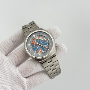May include: A silver-toned stainless steel wristwatch featuring a round case and a link bracelet. The dial displays a colourful world map graphic with blue and orange segments, a 24-hour numerical ring, and the Edox brand name printed at the bottom.