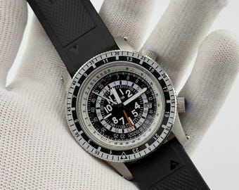 May include: A wristwatch with a black rubber strap and a silver-tone metal case. The round black dial features white Arabic numerals, a date window, and an orange second hand. A rotating bezel with black markings surrounds the dial, which displays the text FORTIS.