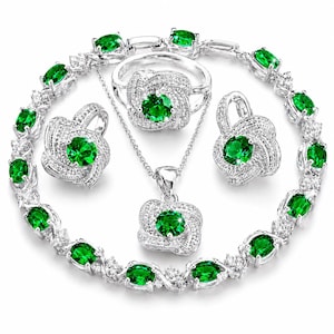 May include: A jewelry set consisting of a silver-toned necklace, a ring, a pair of earrings, and a bracelet. Each piece features a central round-cut emerald green stone surrounded by a cluster of small clear crystals in a knotted metal setting.