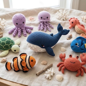 Puede incluir: Una colección de criaturas marinas de ganchillo que incluye una ballena azul oscuro, una tortuga verde, un pez payaso naranja y negro, un cangrejo rojo, un pez azul, un pulpo morado, una medusa lila y un caballito de mar naranja, con conchas.