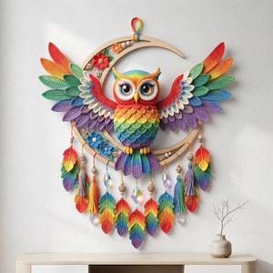 May include: A wall hanging featuring a crocheted rainbow owl with large eyes, perched on a wooden crescent moon frame. The owl has spread wings and a tail made of colourful feathers, accented with hanging tassels, beads, and clear crystal prisms.